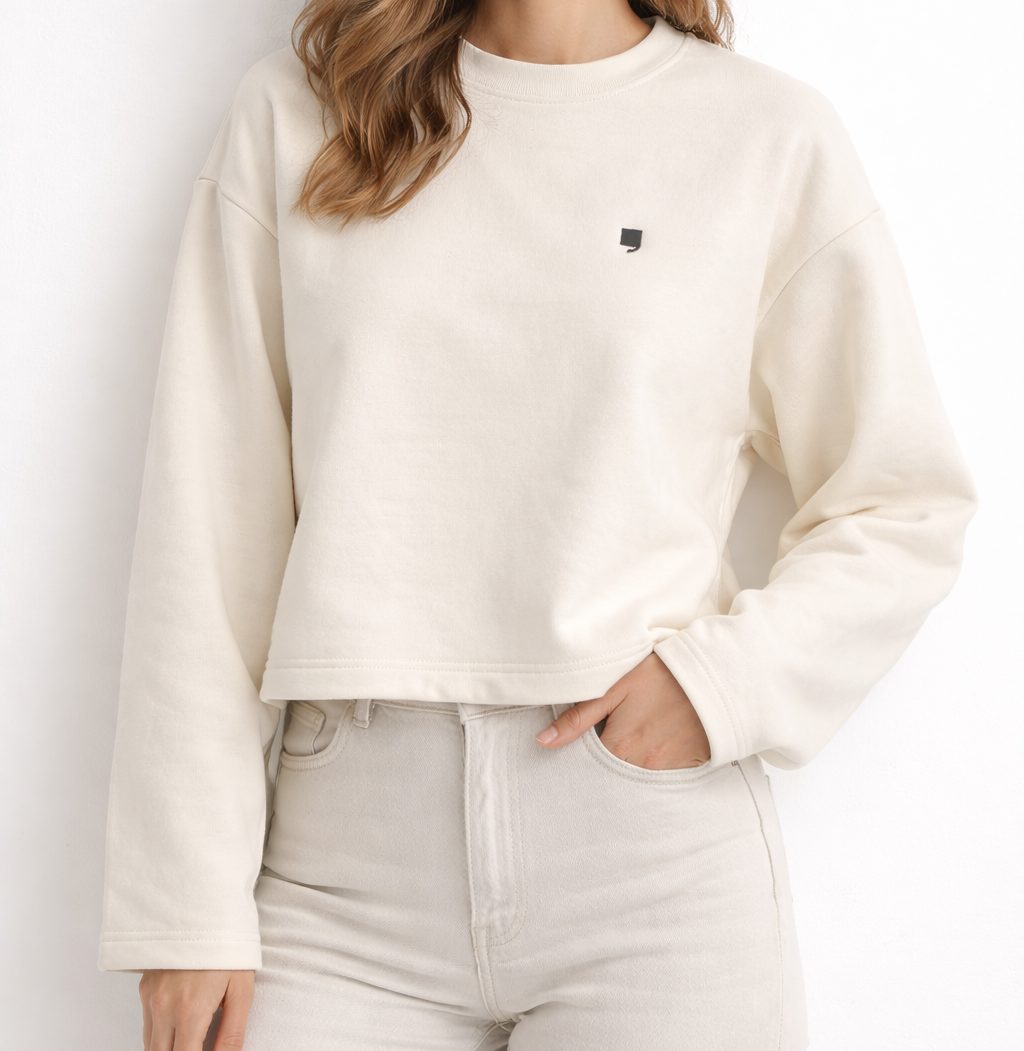 Woman wearing a beige sweatshirt with a small black logo against a white background